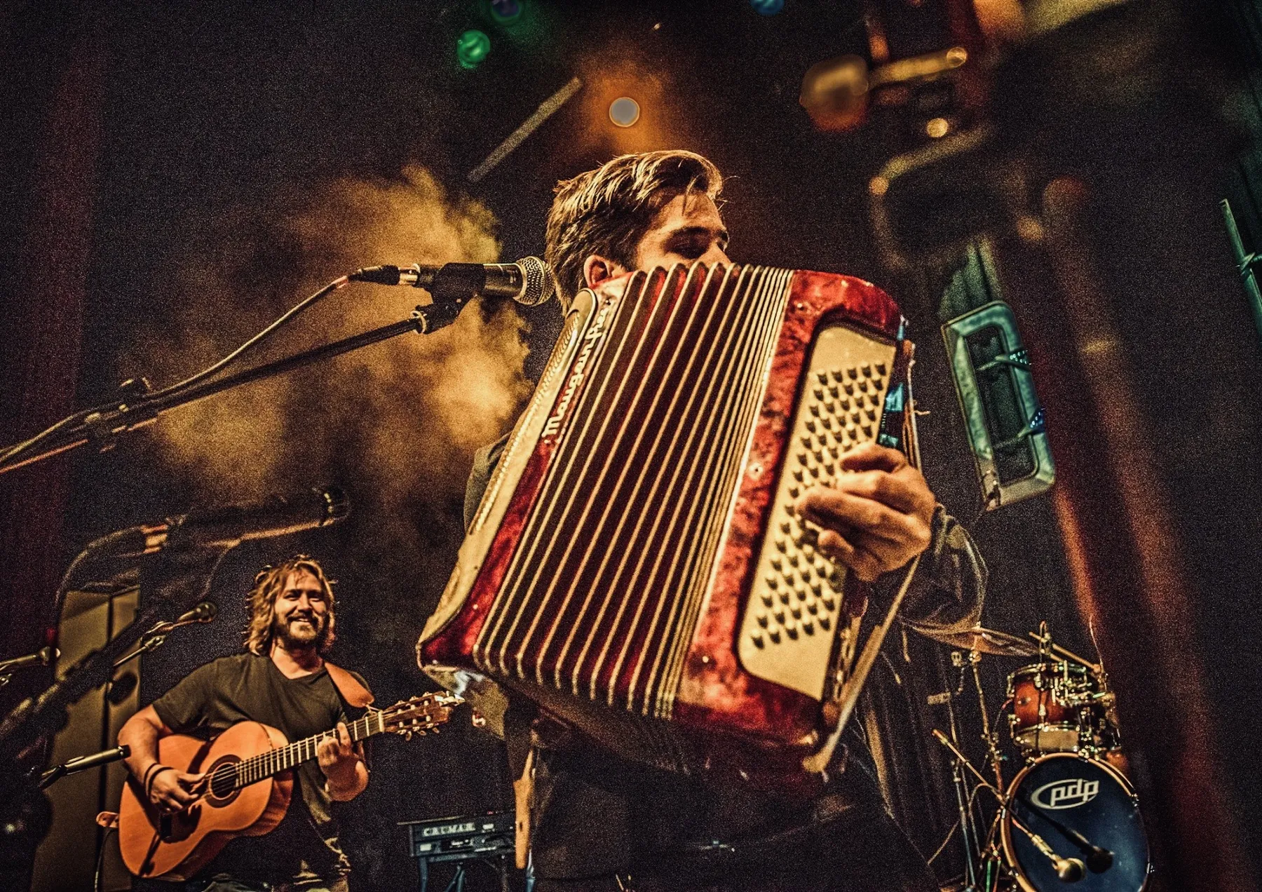 Chris & Pierrot sur scène dans une lumière ambrée : au premier plan, l'accordéon rouge ; derrière, une guitare acoustique.
