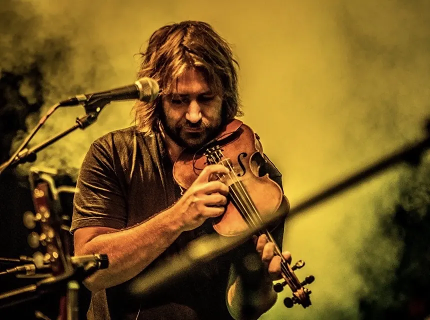 Chris joue du violon au micro, dans une lumière jaune.
