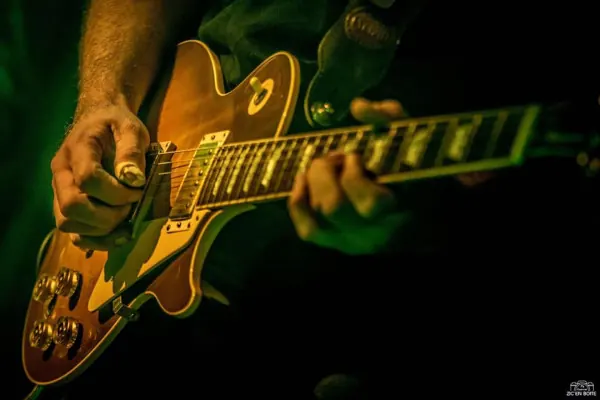 Nico à la guitare : gros plan sur ses mains et une guitare électrique ambrée.